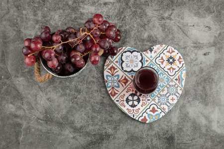 Metal bucket of red fresh grapes and glass of juice on marble tableの写真素材