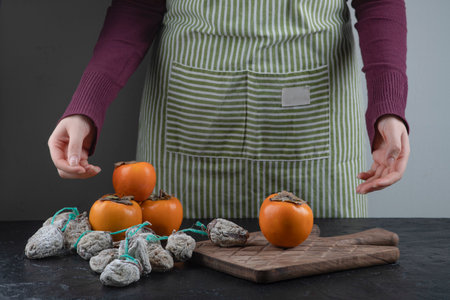 Female cook trying to pick fresh or dry persimmons on black tableの写真素材