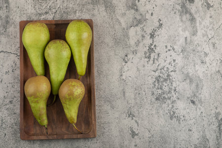 Wooden plate of delicious ripe pears on marble background
