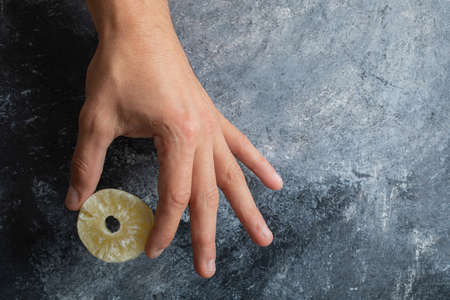 Male hand holding dried pineapple ring on marble backgroundの写真素材