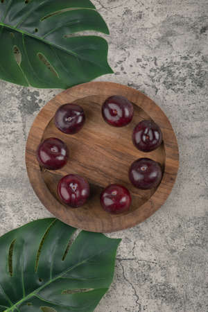 A wooden plate of fresh purple plums with green leavesの写真素材