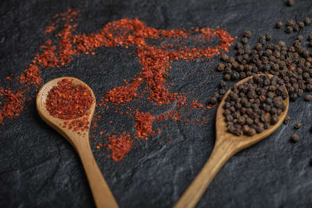 Red and black peppercorns with wooden spoon over black backgroundの写真素材