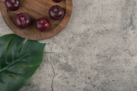 A wooden plate of fresh purple plums with green leaves