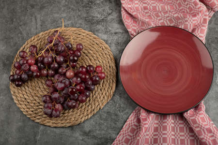 Cluster of red grapes and empty red plate on marble surfaceの写真素材