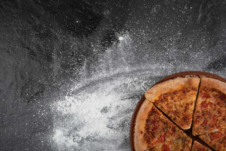 Homemade sliced pizza on brown plate on black surfaceの写真素材