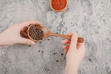Female hands holding wooden spoon of pepper grains on marble backgroundの写真素材