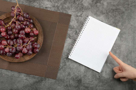 Cluster of red grapes on wooden plate and empty paper on marble surfaceの写真素材