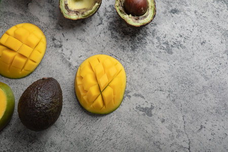 Sliced tropical fruit mango and broken avocado on marble surface