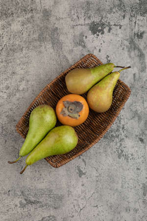 Delicious fuyu persimmon and ripe pears in wicker basketの写真素材