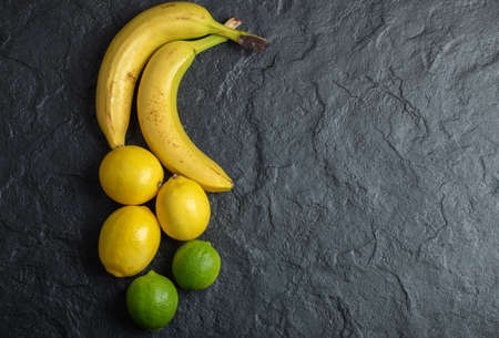 Top view of pile of fresh organic fruits over black background. Bananas and lemonsの写真素材