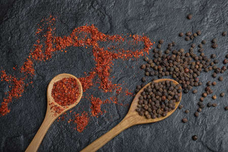Red and black peppercorns with wooden spoon over black background