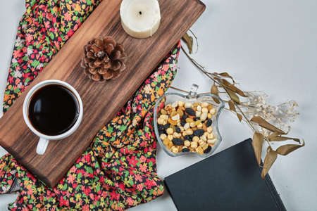 A cup of coffee with candle, forest cone, nuts on the wooden board