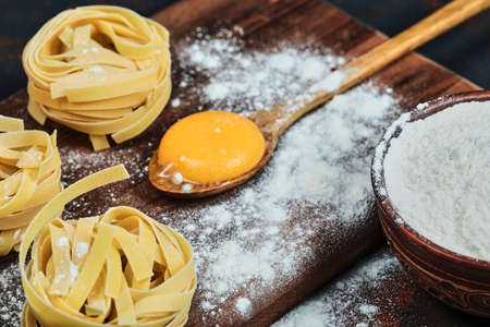 Raw tagliatelle pasta on wooden board with bowl of powderの写真素材