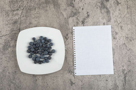 White plate of delicious fresh blueberries and paper on marble surfaceの写真素材