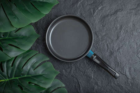 Top view of frying pan over black background with green leavesの写真素材