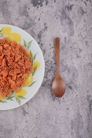 Plate of heart shaped raw macaroni and wooden spoon on marble backgroundの写真素材