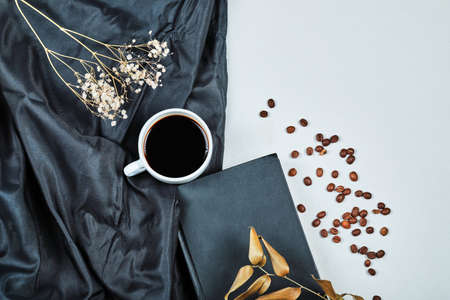 A cup of coffee with flower and book on the dark cloth