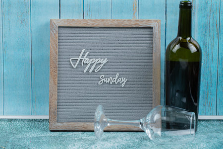 Happy sunday poster embedded on grey background with a bottle of wineの写真素材