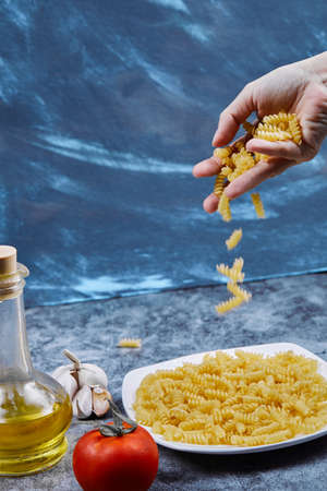 Woman pours raw fusilli into the plate with tomato, garlicの写真素材