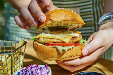 Hands holding fresh delicious burger with french fries and salad on wooden tableの写真素材