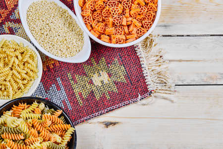 A bunch of colorful uncooked pasta bowls on wooden table with carved cloth
