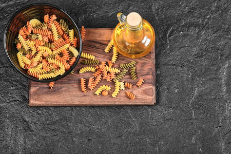 Bowl of colorful fusilli pasta and bottle of oil on dark tableの写真素材