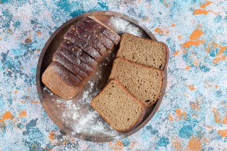 Slices of brown bread with flour on a wooden round boardの写真素材