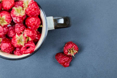 Fresh red raspberries in mug on blue background