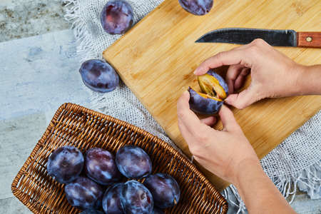 Holding fresh plum on wooden board with basket of plumsの写真素材