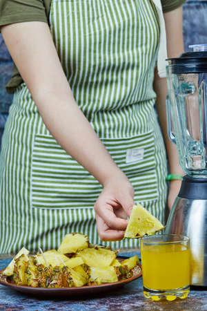 Hand holding a slice of pineapple on blue backgroundの写真素材