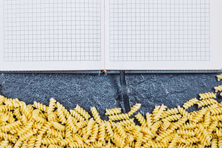 Scattered raw pasta around notebook on blue backgroundの写真素材