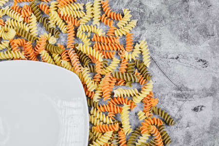 Colorful fusilli and white plate on marble backgroundの写真素材