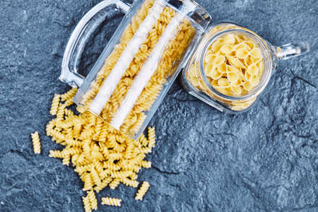 Raw pasta inside the two glass jars on blue background