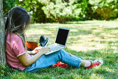 Young woman sitting on green grass while using laptopの写真素材