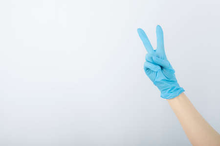 Hand wearing surgical glove and showing victory gesture