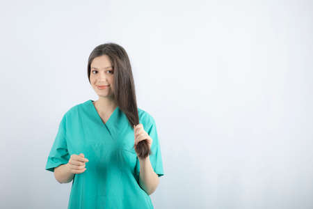 Young beautiful nurse plaiting her hair while looking at cameraの写真素材