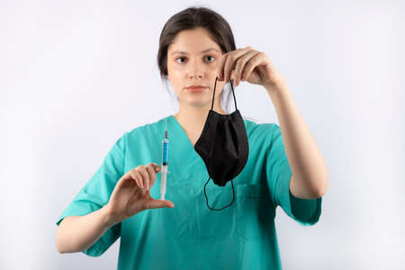 Young beautiful nurse holding injection and mask on hand while looking