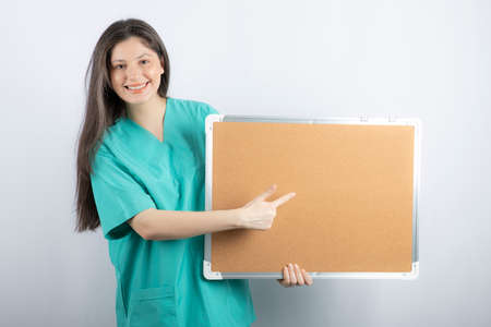 Smiling medical worker holding board and pointing finger on it