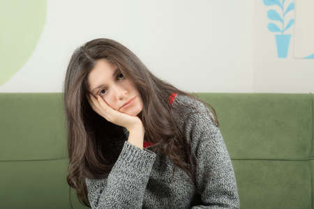 Tired young beautiful girl sitting on the sofa and holding her hand to her head