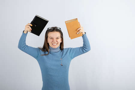 Portrait of a girl in eyeglasses holding two books on white-gray background