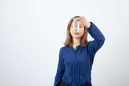 Portrait of young adorable girl looking at glass of water on white background
