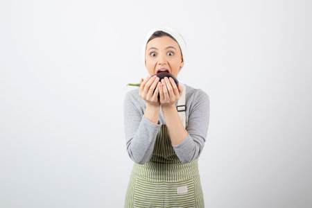 Picture of a nice young woman model in apron eating an eggplantの写真素材