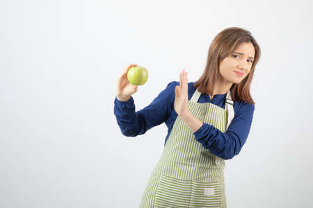 Photo of a cute young woman model in apron refusing from a green fresh apple