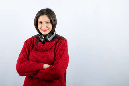 A young smiling woman in red warm sweater standing with headphonesの写真素材