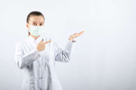 Woman doctor in white uniform wearing a medical mask and pointing awayの写真素材
