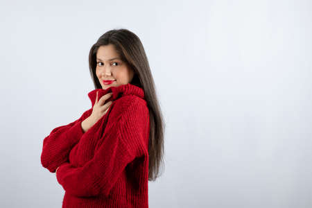 Portrait photo of a young woman model in red warm sweater standing and posingの写真素材
