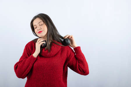 A young smiling woman in red warm sweater standing with headphonesの写真素材