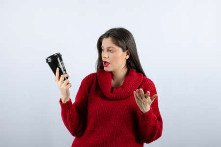 A young woman model in red sweater looking at a cup of coffeeの写真素材