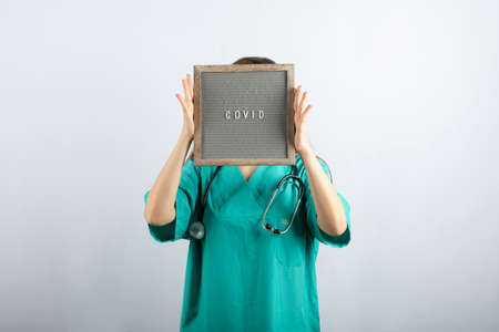 Young nurse in medical mask with stethoscope covering face with a frameの写真素材