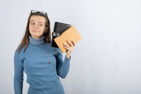 Portrait of a girl in eyeglasses holding two books on white-gray backgroundの写真素材